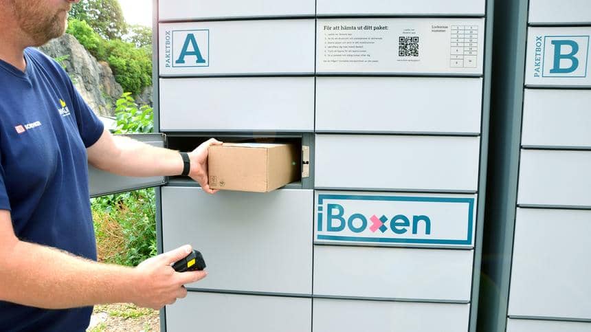 En man lägger ett brunt paket i en stor leveransbox med logga iBoxen.