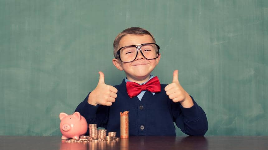 En glad pojke i stora glasögon visar tummen upp sittandes framför en spargris och en hög med mynt.
