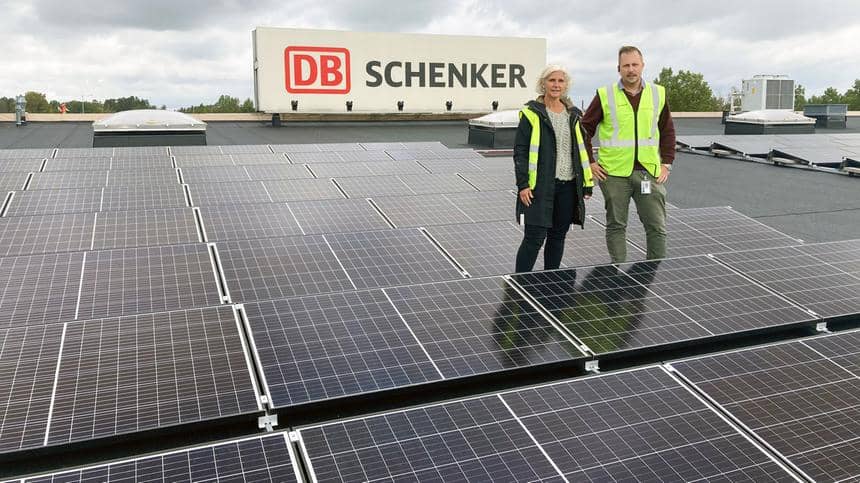 Två personer i reflexkläder bredvid DB Schenker-logotyp står framför stora solceller.