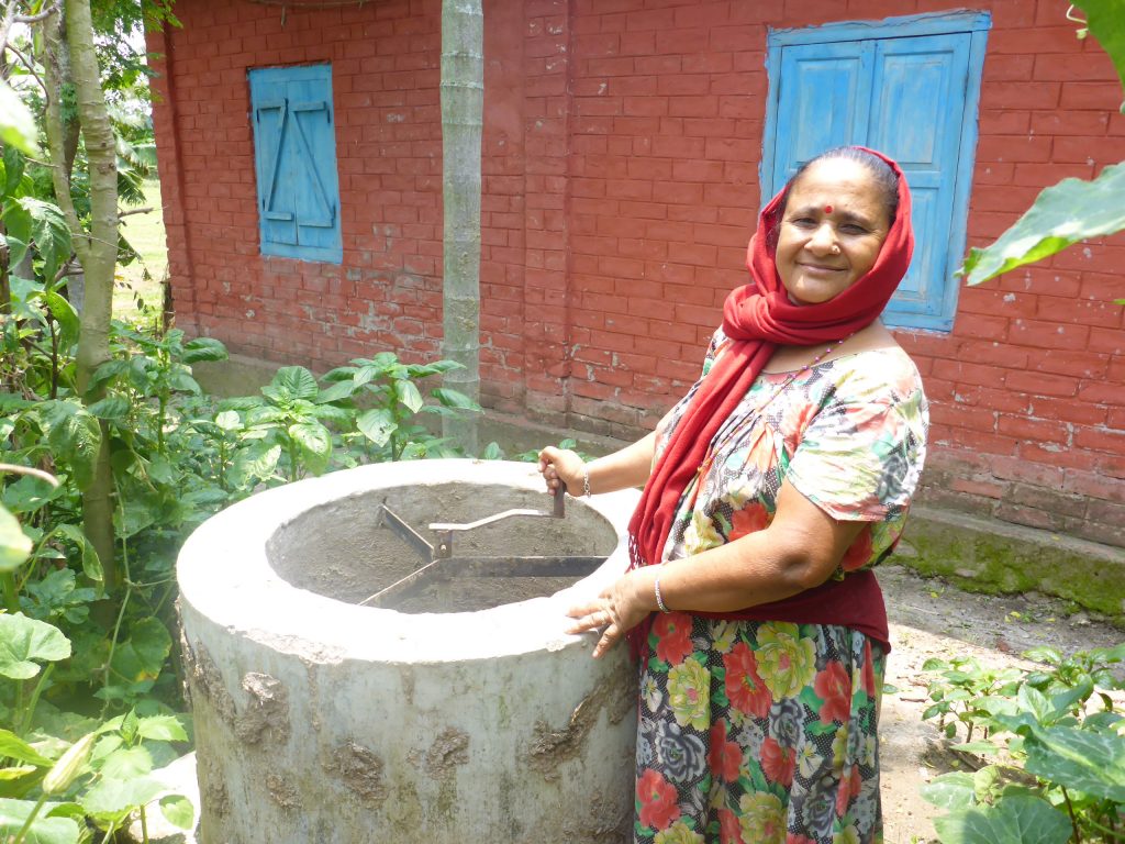 Leende äldre nepalesisk kvinna står vid en biogasanläggning.