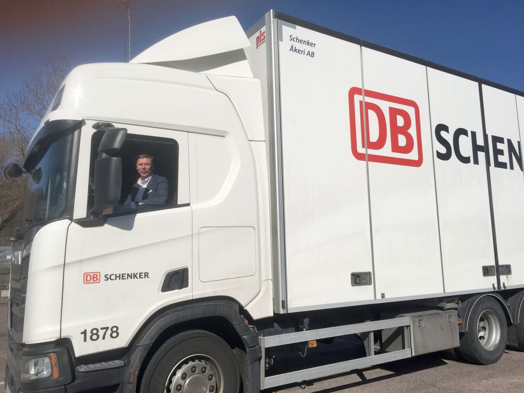 Medelålders man sitter bakom ratten i en vit lastbil med DB Schenkers logotyp.