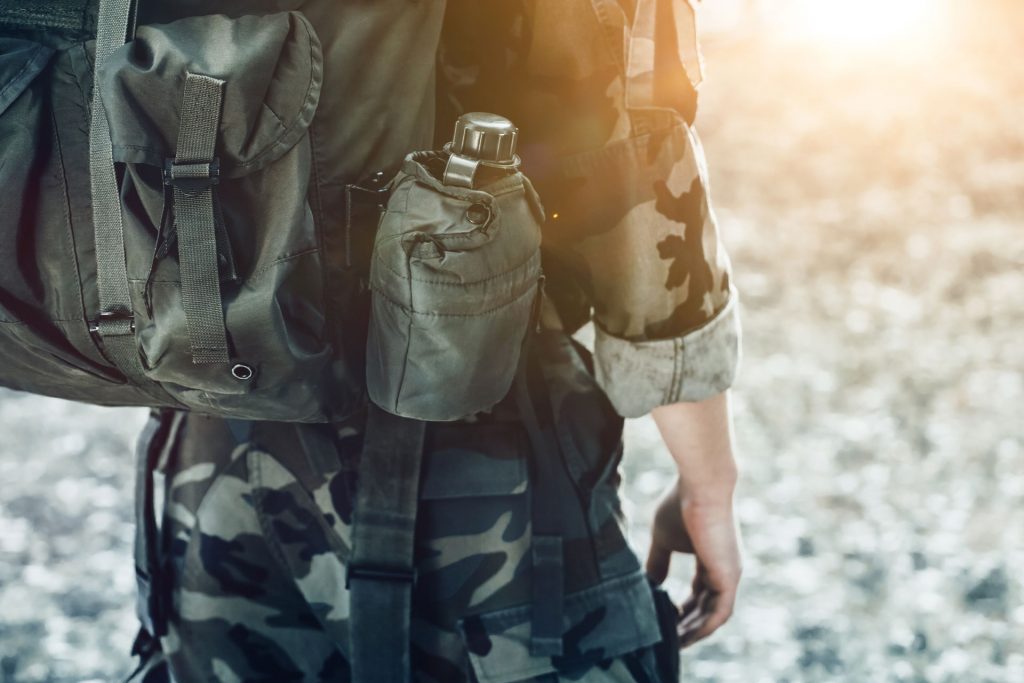 Beskuren bild av en person klädd i militärkläder med ryggsäck och vattenflaska.